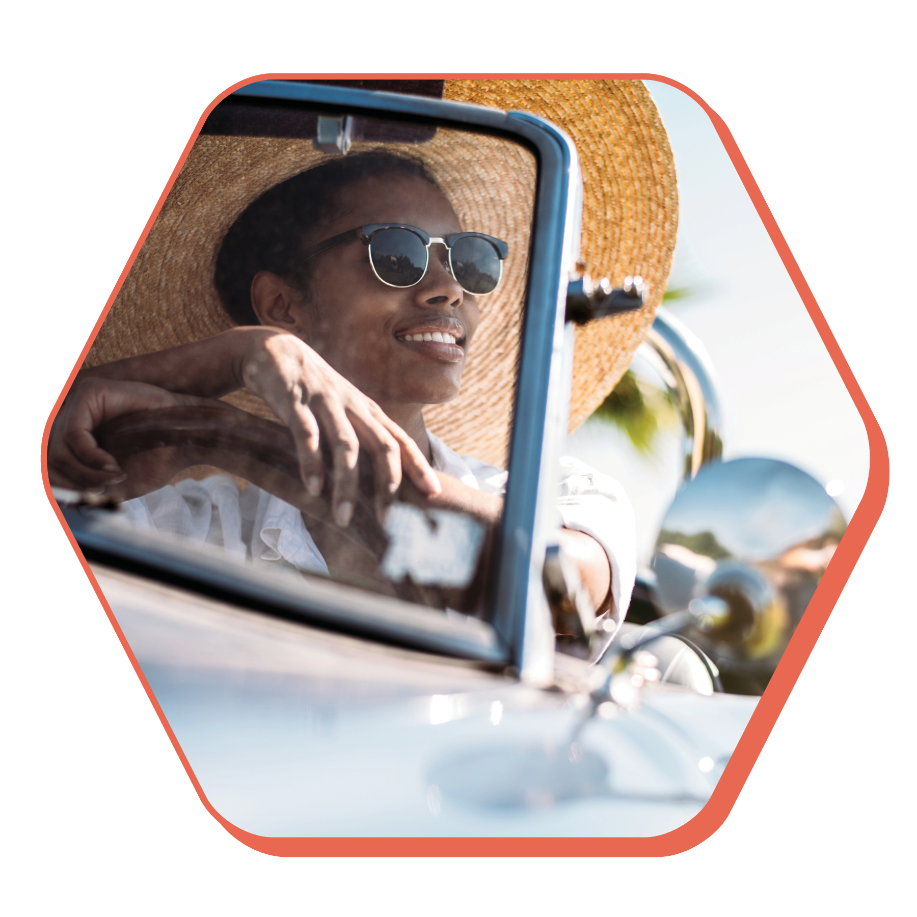 Young woman with dark skin, sunglasses, and wide brimmed hat smiles as she sits in the driver's seat of a vintage convertible on a sunny day